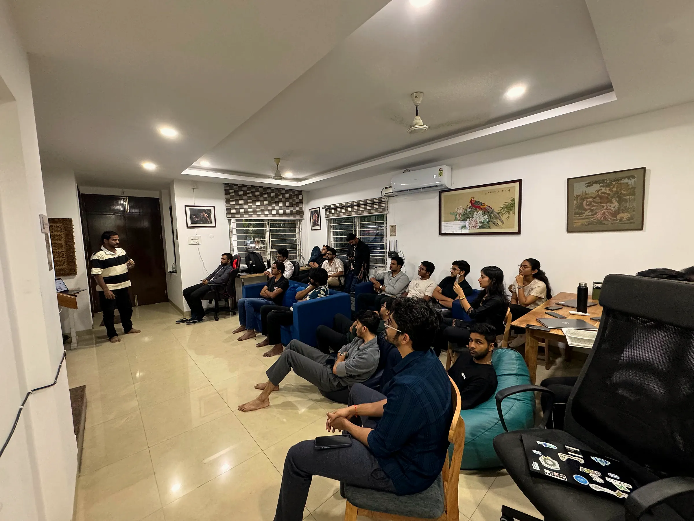 The living room full of people watching a founder present at a weekly demo